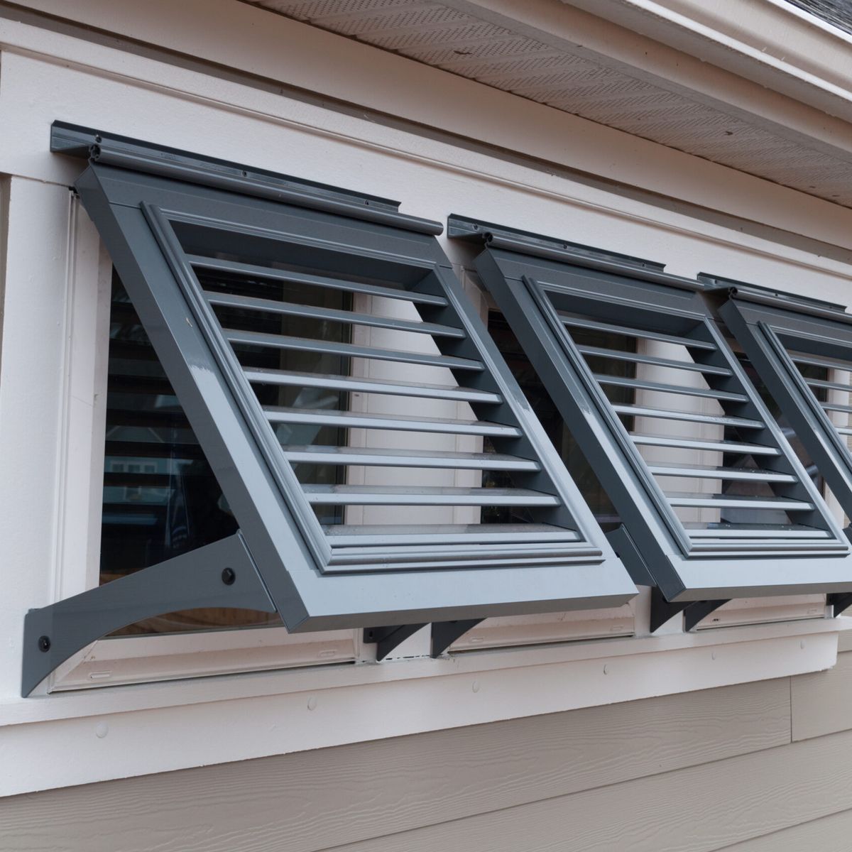 Three louvered metal storm shutters on a tan siding wall