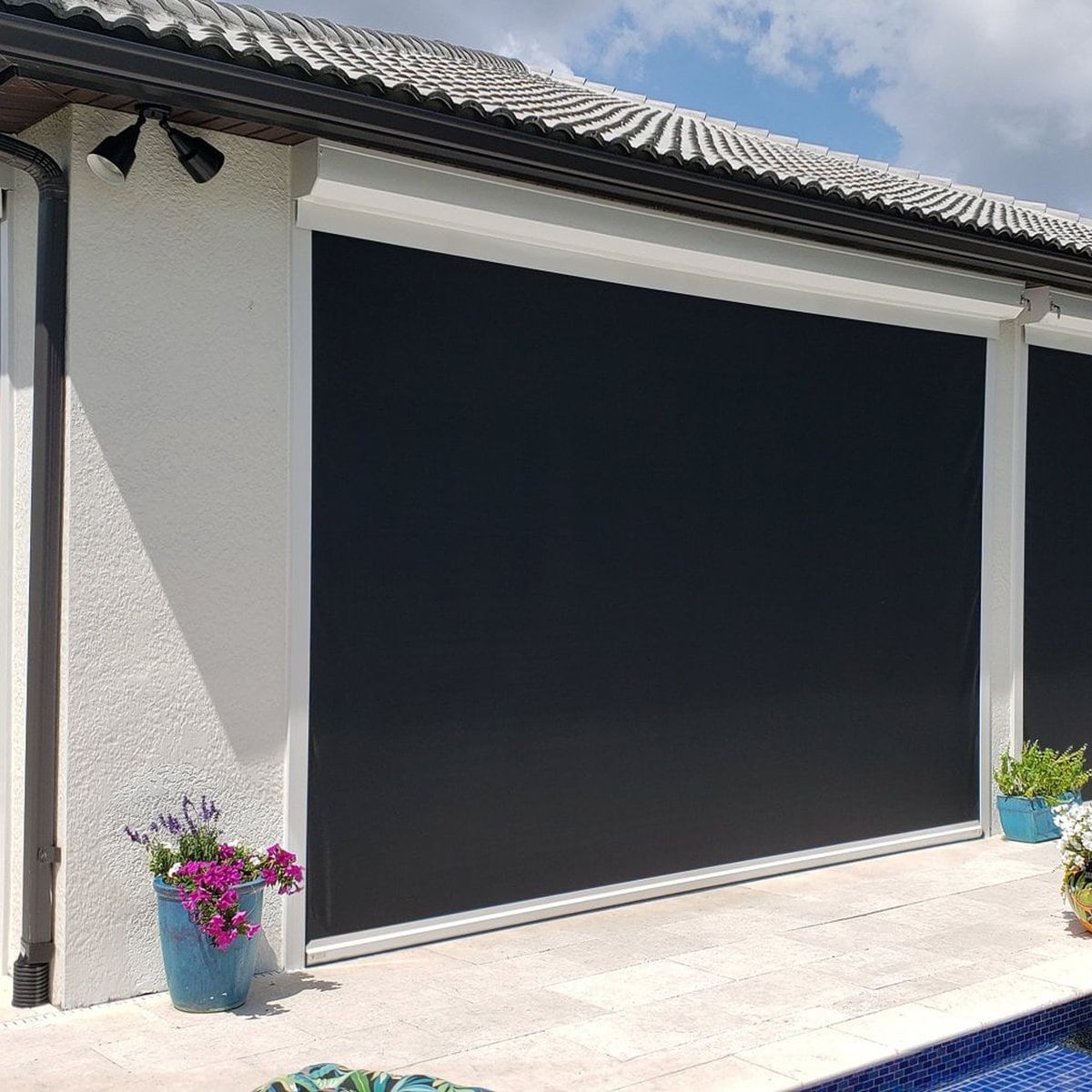 Three motorized screens lowered across a white stucco pool house